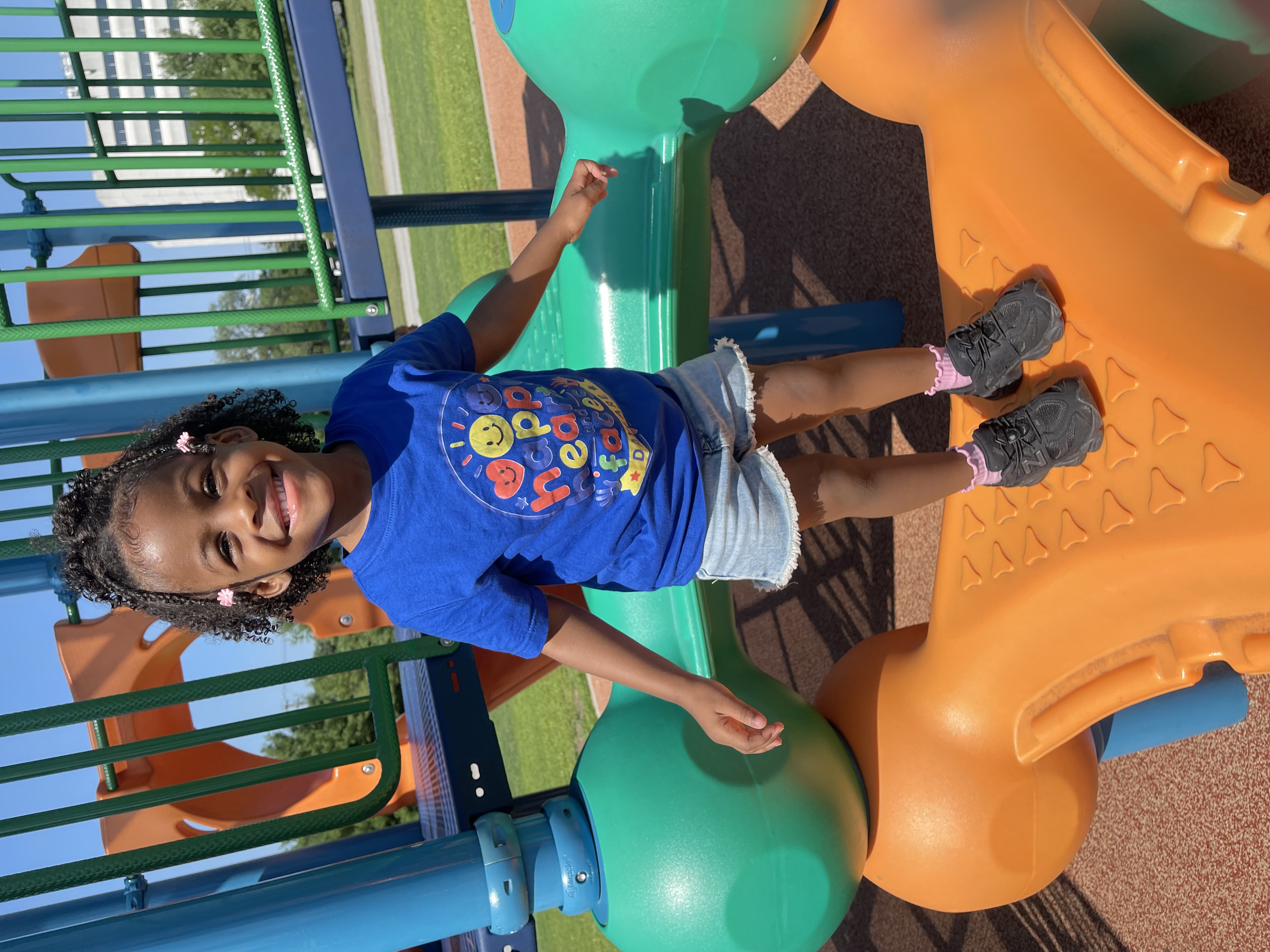 Girl in a Happy Hearts and Faces Daycare shirt smiling on the playground